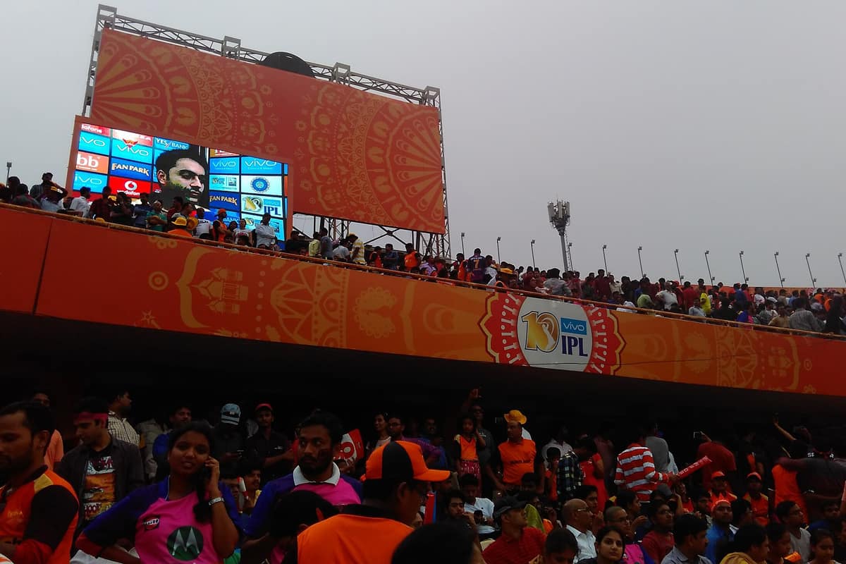 A digital scoreboard showing "287/3" with a blurred stadium background.